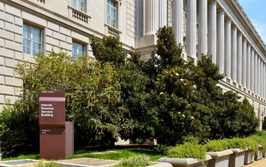 WASHINGTON, DC, USA - MARCH 4, 2012: A woman walks by the Internal Revenue Service building in Washington, DC. A small IRS sign in the corner of the building contrasts with its massive, neoclassical architecture.